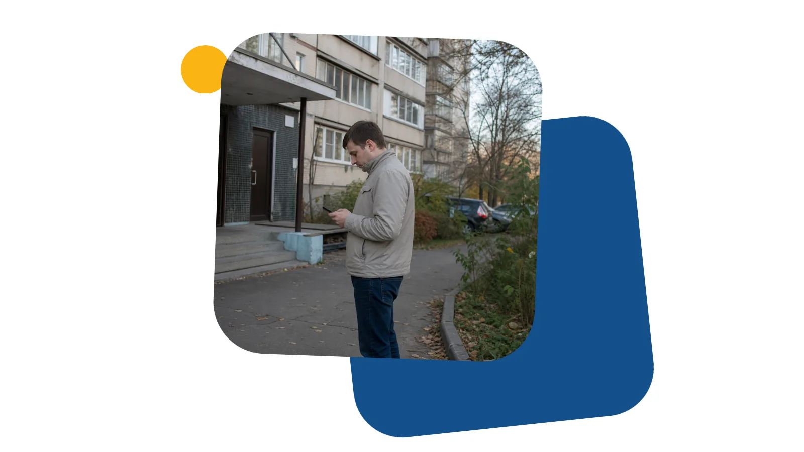 Молодий чоловік стоїть біля під'їзду з телефоном у руці і дивиться на екран