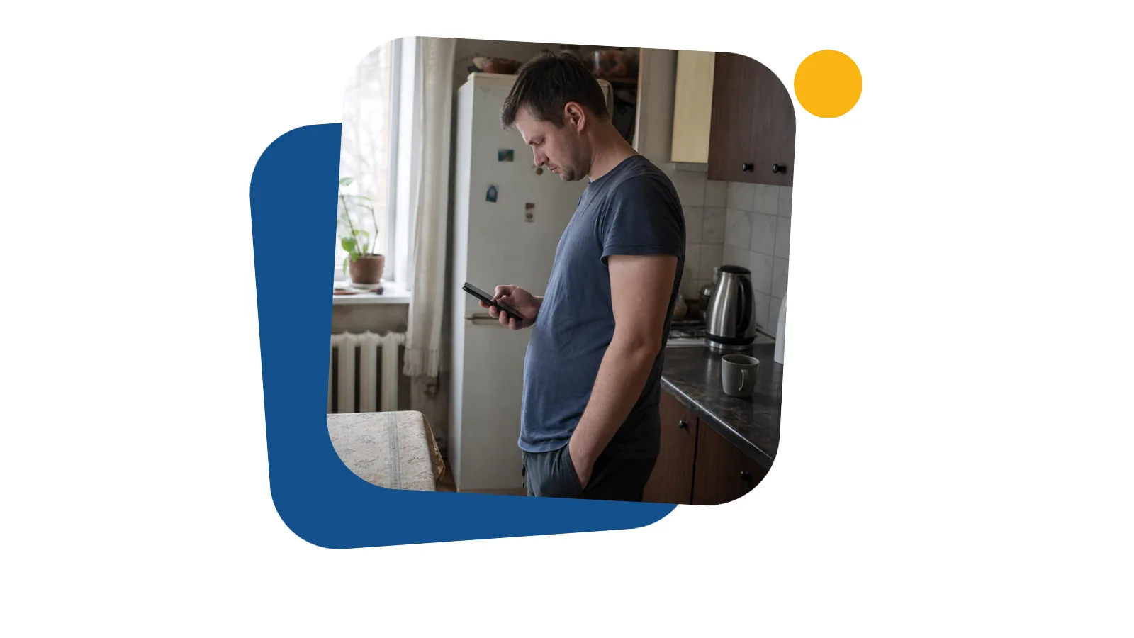 Чоловік на кухні орендованої квартири читає повідомлення на телефоні і хмуриться